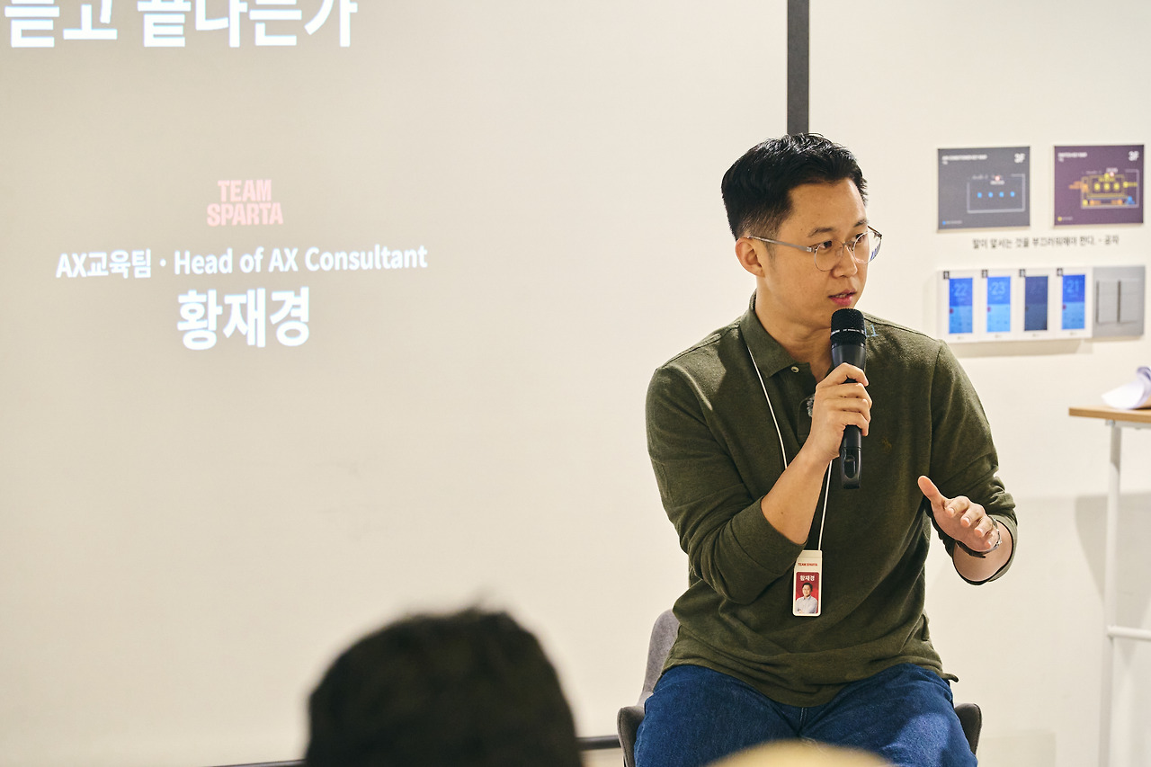 마이크를 들고 답하는 게스트 연사와 옆 스크린의 소속·직함 자막